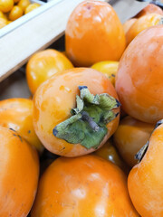A persimmon with leaves lies in a box in close-up. A bright background for advertising a fruit and vegetable market. Wallpaper for the screen. 