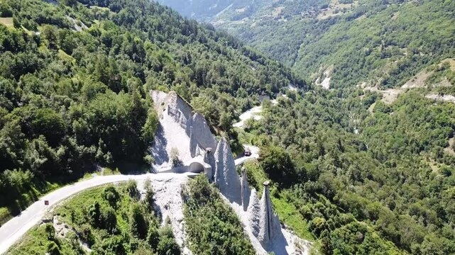 Aerial view of the Pyramides d&rsquo;Euseigne, showcasing unique earth pyramids surrounded by lush green forests and winding roads, as the drone circles around the natural formations