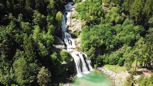 Aerial view of the stunning Piumogna waterfall flowing down a rocky cliff face, surrounded by vibrant green forest in Faido, Switzerland on a sunny summer day, Ticino canton.