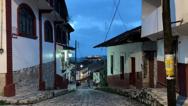 Cobblestone street with colonial-style architecture under a dim, blue sky in a historic Mexican town Cuetzalan belonging among Pueblos Magicos.