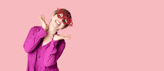 A cheerful young woman in Christmas glasses poses on a highlighted pink background.
