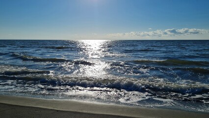 Sea waves roll onto the sandy shore, the glare of the sun plays on the water