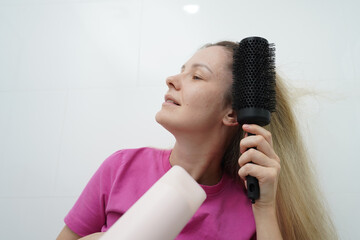 A woman is expertly styling her hair using a blow dryer and brush while in the bathroom