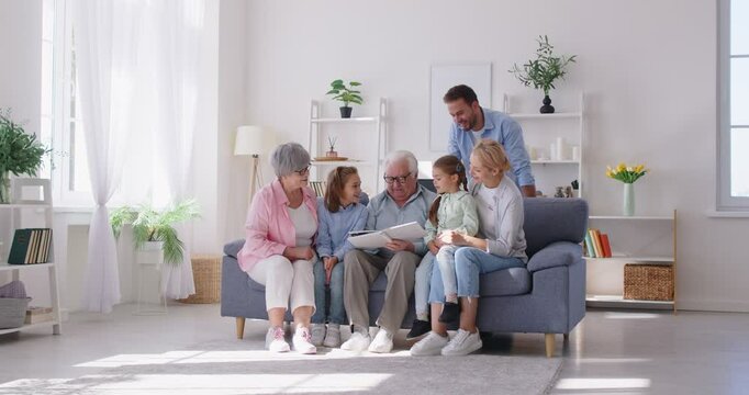 Happy family sitting together on a sofa at home, enjoying leisure time by looking at a photo album. The family shares memories and remembrances, creating a moment of togetherness and happiness.
