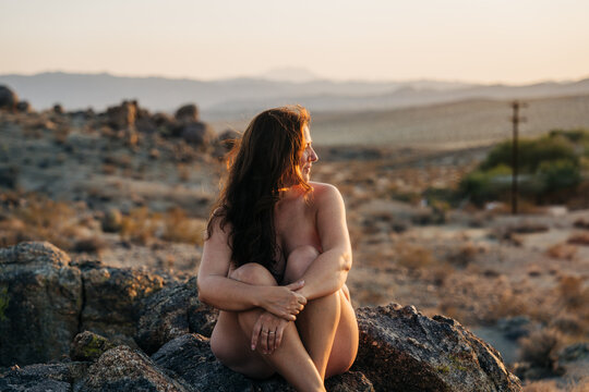 Woman seated on desert rocks at sunset, gazing into the distance