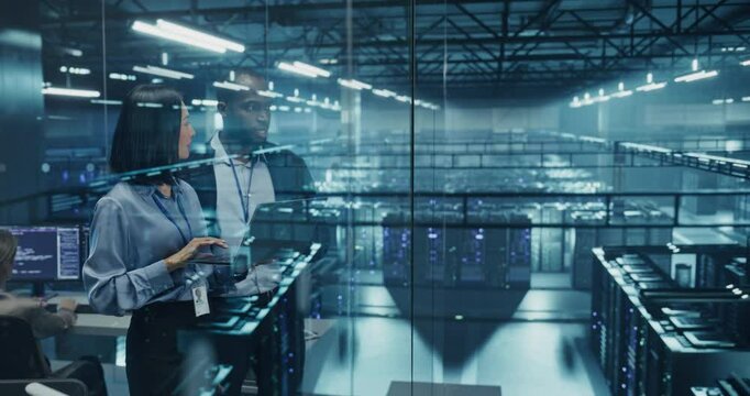 Male DevOps Engineer and Female IT Consultant Work on a Laptop Computer, Standing in an Office Above the Supercomputer with Server Cluster, Developing Automation Scripts for Artificial Intelligence