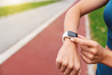 Runner’s wrist with smartwatch tracking health metrics on blurred running trail background.