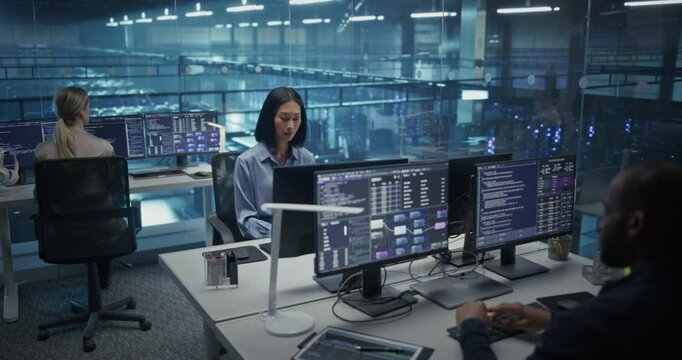 In a Data Center Office With Glass Walls, Diverse Female and Male Team Members Focus on Their Desktop Computers, Conducting Routine System Checks and Working on Network Improvements