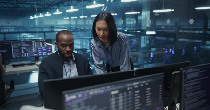 Black Male and Asian Female Engineer Collaborate on a Project in a Modern Data Center Office. Specialists Analyzing Complex Systems on Multiple Screens to Improve Cybersecurity and Performance