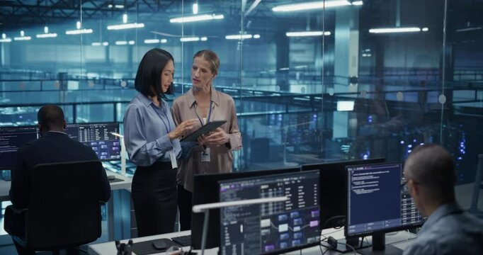 In a Modern Data Center, Caucasian Female Data Scientist and Asian Female AI Specialist Analyze Algorithms on a Tablet Computer. Specialists Exploring Optimizations for Processing Large Datasets