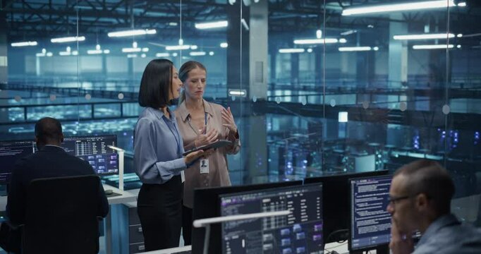 Two Diverse Female Cloud Security Engineers Work Side by Side on a Tablet Computer in a Data Center Office, Conducting a Thorough Security Audit of the Server Network Infrastructure