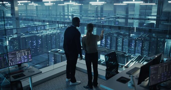 In a Modern Data Center, Black Male Data Scientist and Female AI Specialist Analyze Algorithms on a Tablet. Specialists Exploring Optimizations for Machine Learning Models Processing Large Datasets - Powered by Adobe