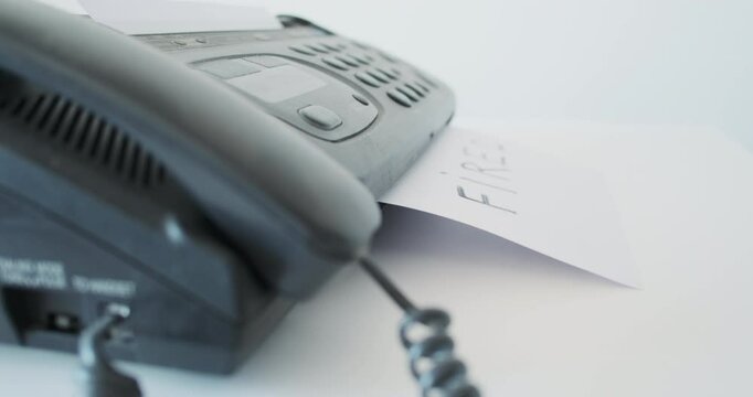 Fired, fax machine prints message on paper, side view. Concept notice of dismissal from work, global crisis, market collapse.