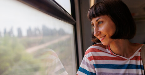 train travel. Young pretty woman enjoying a train ride, sitting near the window and looking out the window.  Enjoy your travels.