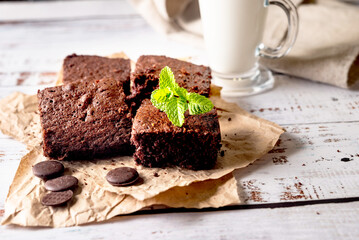 Many pieces of fresh chocolate brownie sprinkled with cocoa on a  bakery paper with glass of milk...