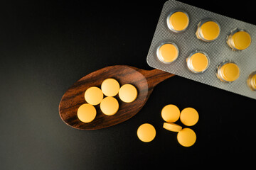 Pills Medicine tablet capsules blister pack in wooden spoon on a black background