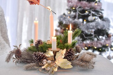 A woman lights the last Advent candle.Four Advent candles are burning.