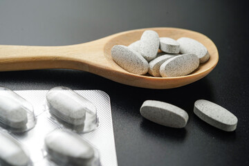 white Pills Medicine tablet capsules in a wooden spoon blister pack on a black background