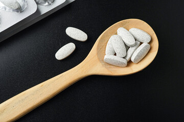 white Pills Medicine tablet capsules in a wooden spoon blister pack on a black background