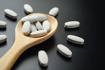 white Pills Medicine tablet capsules in a wooden spoon blister pack on a black background