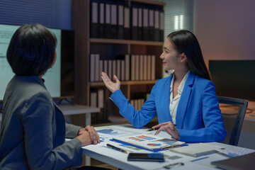 Two Asian businesswomen come up with an idea. Discuss investment projects and strategic planning with information via various documents and files. On a laptop computer at modern office.