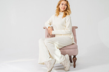 Attractive young blonde girl sits in a pink chair, white background, copy space