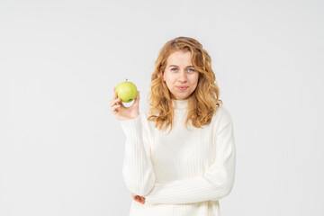 Happy attractive blonde young girl holding a green apple, white background, copyspace