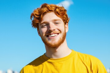 Smiling young man with red hair against a clear blue sky background
