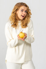 Happy attractive blonde young girl holding a yellow pear, white background, copyspace