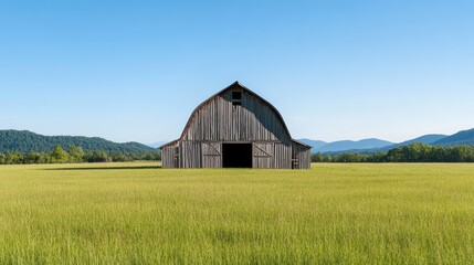 Obraz premium A scenic view of a rustic barn surrounded by lush green fields and mountains under a clear blue sky.