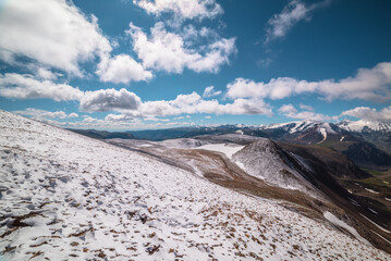 Snowy stony pass, large colorful mountain range and valley in far away. Snow-white glacier in...