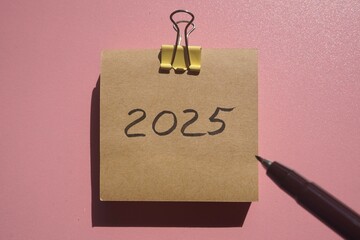 craft memo pad sticky note with the inscription 2025 and clip and dry flowers plant on a pink...
