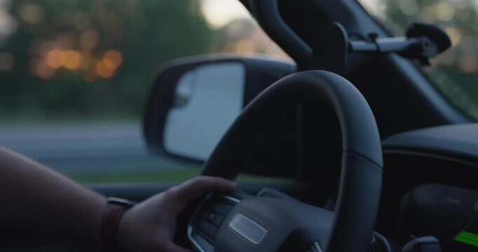 Close up on male hand driving steering wheel of SUV or private vehicle down a highway at sunset or sunrise. Freeway ride as man driver has his hand on black steering wheel of pick up truck going fast