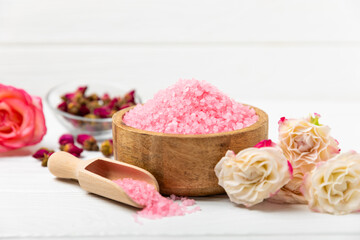 Sea salt for bath with aroma and rose flowers on textured wooden background. Pink sea salt. Spa treatments. Natural salt with herbs and essential oils. skincare concept. Meso for text. Copy space