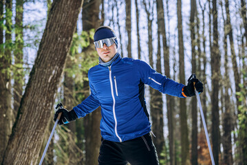 Male athlete practicing cross-country skiing in a snowy forest, enjoying winter sports and exercising outdoors amidst nature