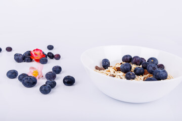 Bowl of rolled oats with fresh blueberries and scattered berries on a white background, capturing a healthy and minimalist breakfast