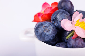 Fresh blueberries and vibrant red and pink flowers in a bowl, displayed on a white background with a refreshing and detailed close-up view