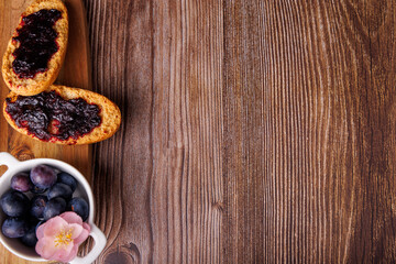 Delicious toast spread with blueberry jam and a butter dish on a wooden cutting board, presented on a dark wooden table from above