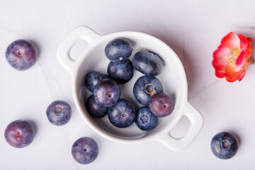 Overhead view of a white marble table featuring a porcelain container full of blueberries, surrounded by scattered berries for a fresh and colorful display