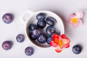 A beautiful top-down view of blueberries scattered on a white marble table, featuring a porcelain bowl filled with juicy blueberries for a fresh look