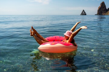 Summer vacation woman in hat floats on an inflatable donut mattress. Happy woman relaxing and...