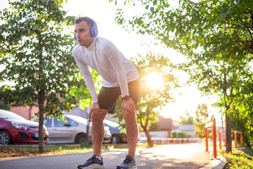 Young sporty man taking break after running in city park