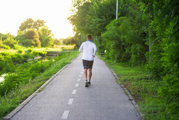 Young man running on a park road at sunset