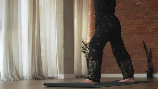 Beautiful shot of girl's barefoot lower body on a yoga mat during the yoga class. Indian style black pants with elephants on. Natural light from the window.