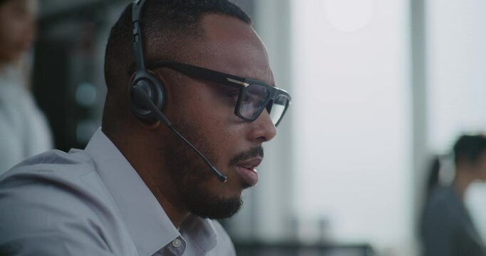 Close up of African American hotline operator in headset having conversation on call with customer, providing online assistance for client. Technical support specialist works in call center office.