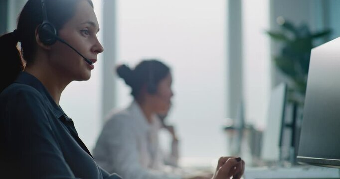 Call center office: Portrait of Caucasian female technical customer support operator working on computer, talking on headset, providing online help for client. Team of helpdesk specialists working.
