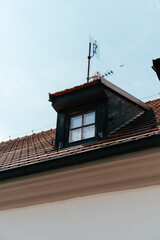 A wooden window on a sloped roof with an antenna in the clear blue sky during bright daylight hours