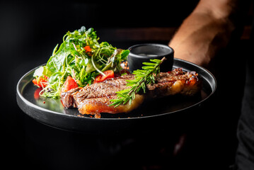 gourmet dish featuring perfectly grilled steak, accompanied by a fresh salad and a side of sauce, elegantly presented on dark plate. Ideal for culinary, food photography, and restaurant menu concepts.