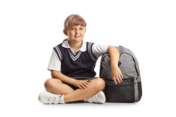 Schoolgirl in a uniform with a backpack sitting on the ground smiling