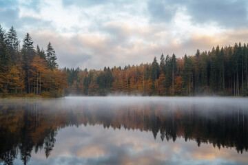 Misty lake reflections surrounded by autumn forest at dawn